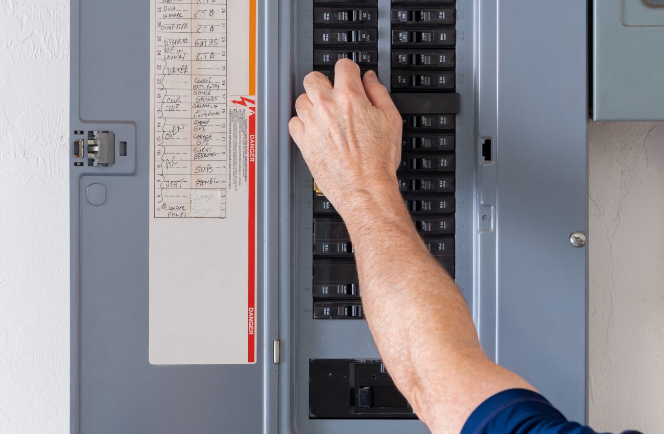 Resetting tripped breaker in residential electricity power panel. Electrician turning off power for electrical outlet at circuit breaker box. Professional electrician checking circuit breaker panel for code compliance